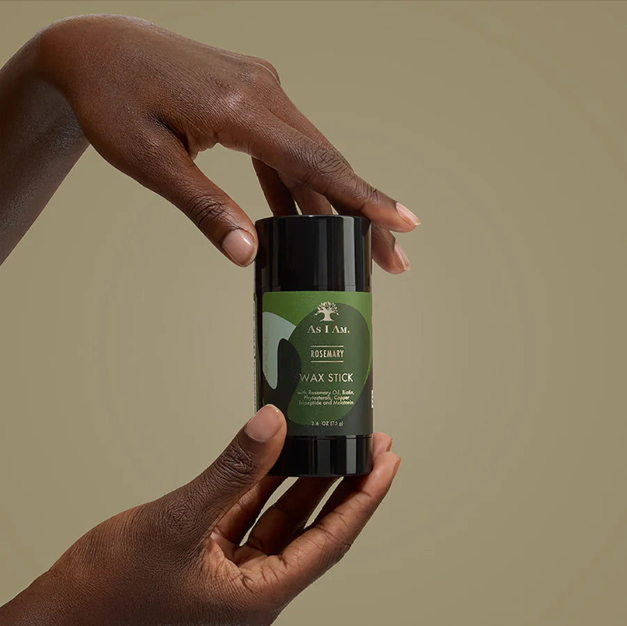 Hand holding a wax stick container with a green label against a beige background