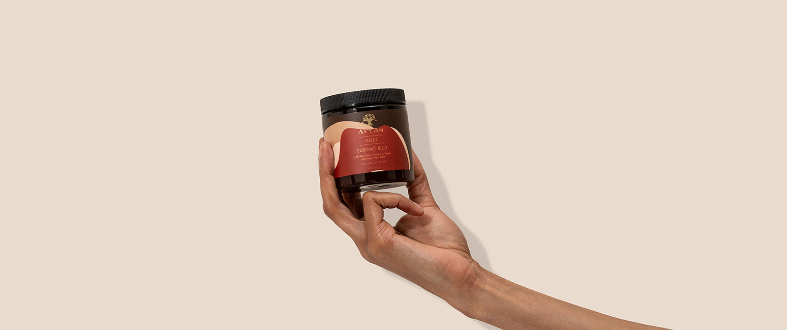 Hand holding a jar with a red label against a beige background