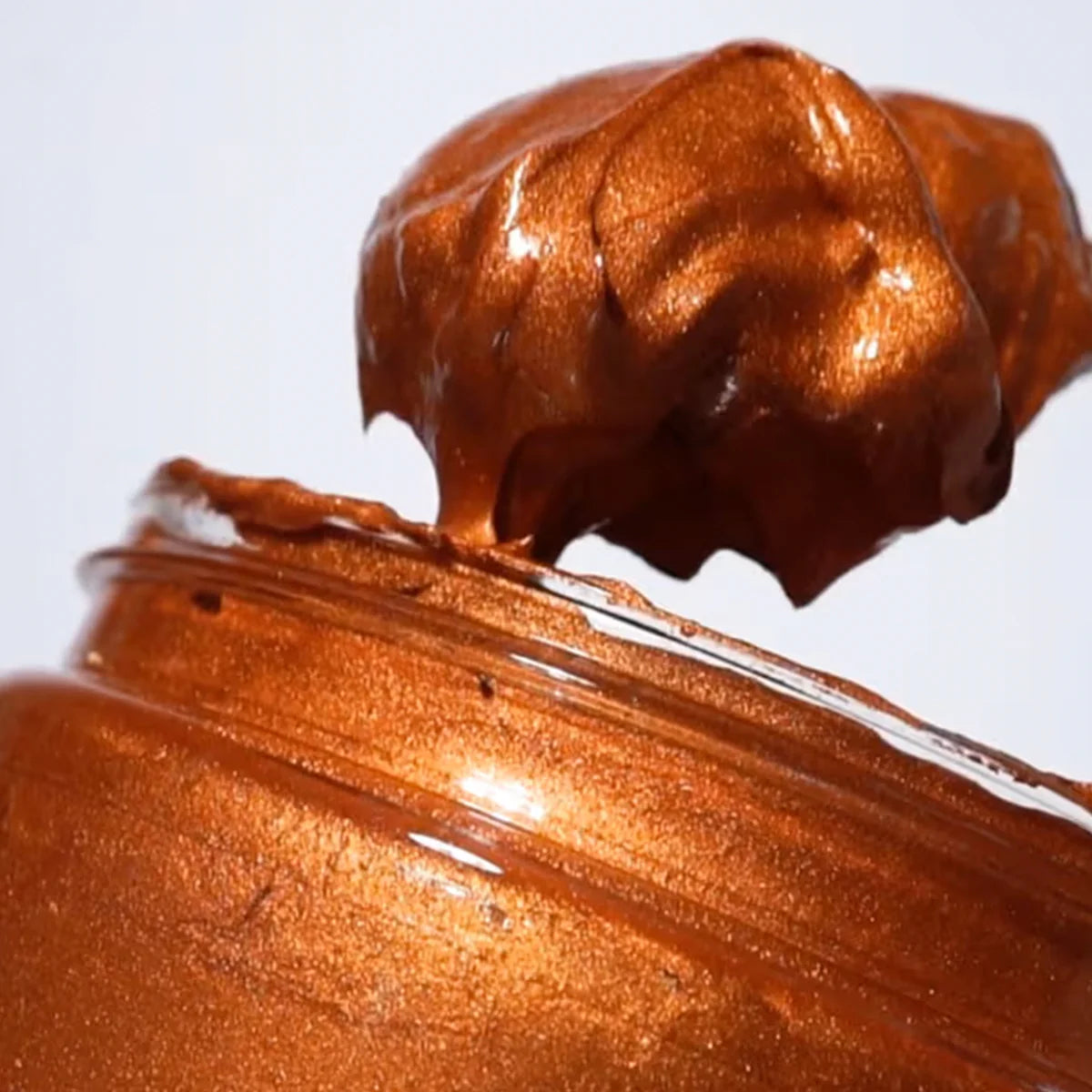 Close-up of a jar of copper-colored cream or spread on a white background