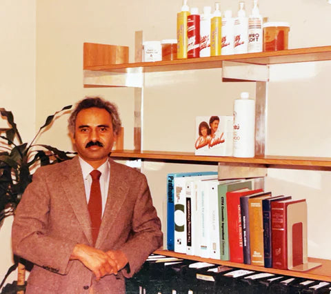 Man in a suit standing in front of a shelf with books and bottles